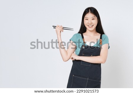 Young Asian woman wearing kitchen apron holding chopsticks isolated on white background.
