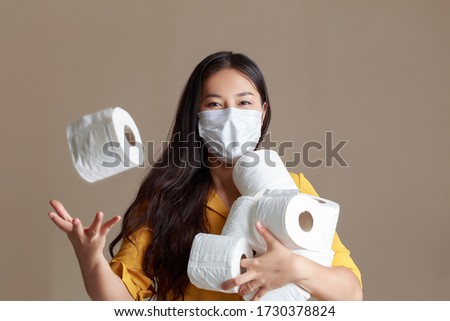 Young Asian woman wearing mask and yellow shirt. Asian woman holding tissue toilet paper during Coronavirus outbreak or Covid-19, Concept of Covid-19 quarantine. people panic.