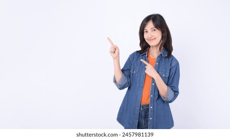 Young asian woman wearing orange t shirt and denim jean while pointing finger to free copy space isolated on white studio background - Powered by Shutterstock