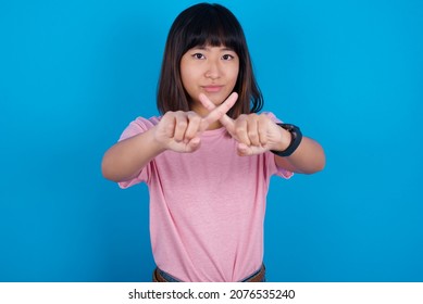 young asian woman wearing pink t-shirt against blue background has rejection angry expression crossing fingers doing negative sign.