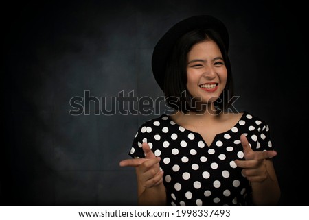 Young Asian woman wearing polkadot dress and hat against dark grey background