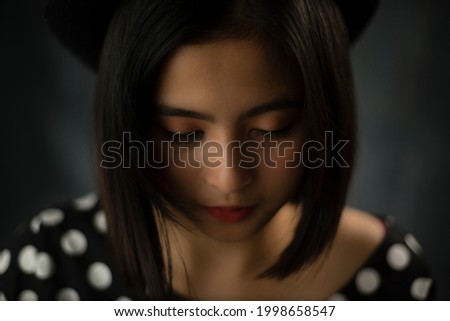 Young Asian woman wearing polkadot dress and hat against dark grey background