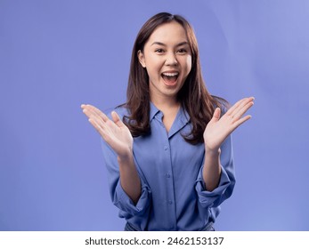 A young Asian woman wearing a purple shirt and jeans stands against a solid lavender background, smiling widely with her arms outstretched, expressing joy and welcoming. - Powered by Shutterstock