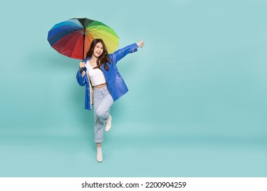 Young Asian woman wearing raincoat and holding rainbow umbrella isolated on green background, In the rainy season concept