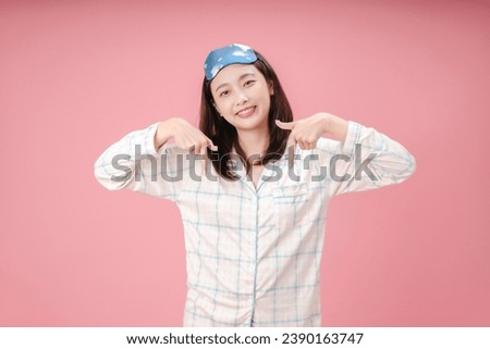 Young Asian woman wearing sleep mask and pajama looking confident with smile on face, pointing oneself with fingers proud and happy.