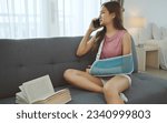 Young asian woman wearing soft splint due to sore arm using phone on sofa at home.