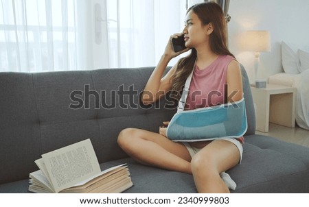 Young asian woman wearing soft splint due to sore arm using phone on sofa at home.