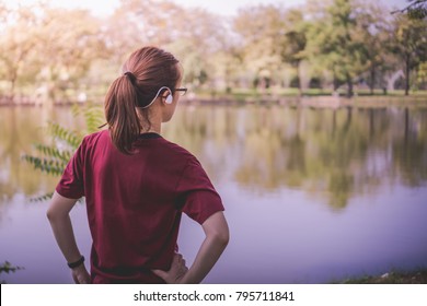 A Young Asian Woman Wearing Sport Ware With Pony Tail Hair Putting Her Arm To Waist Prepare And Ready For Daily Exercise Activity, Running Or Jogging, At The Pond In The Park In A Summer Morning Day