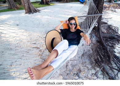 Young Asian woman wearing sunglasses with a pillow resting in comfortable on the hammock at the beach in the sea. The Season of Summer is a relaxation and vacation concept. Travel and holiday. - Shutterstock ID 1965010075