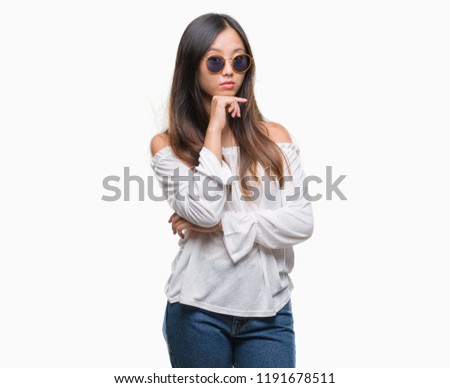 Young asian woman wearing sunglasses over isolated background with hand on chin thinking about question, pensive expression. Smiling with thoughtful face. Doubt concept.