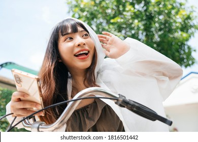 Young asian woman wearing white raincoat holding smartphone shouting on bicycle. - Powered by Shutterstock