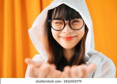 Young Asian Woman Wearing White Raincoat And Eyeglasses Showing Two Hands For Putting Products. Wink Expression.