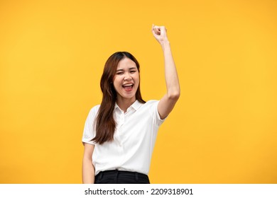 Young Asian Woman Wearing White Short Sleeve Shirt And Raising One Arm While Smiling And Screaming To Celebrate After Successfully Work Isolated Over Yellow Background.