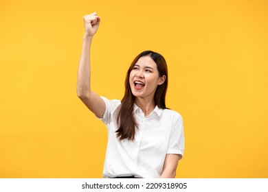 Young Asian Woman Wearing White Short Sleeve Shirt And Raising One Arm While Smiling And Screaming To Celebrate After Successfully Work Isolated Over Yellow Background.