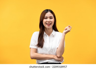 Young Asian Woman Wearing White Short Sleeve Shirt And Smiling To Thinking Something While Crossed One Arm And Raising One Hand Isolated Over Yellow Background.