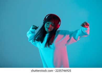 Young Asian woman wearing wireless headphones listening music and dancing in neon light background. Emotions and ad concept	
 - Powered by Shutterstock