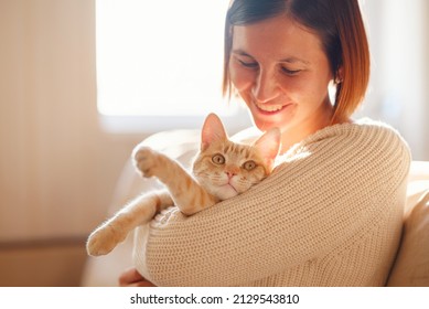 Young Asian Woman Wears Warm Sweater Resting With Tabby Cat On Sofa At Home One Autumn Day. Indoor Shot Of Amazing Lady Holding Ginger Pet. Morning Sleep Time At Home. Soft Focus.