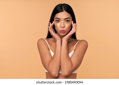 Young Asian Woman In White Lingerie And Clean Radiant Skin With Moisturizing Patches Under The Eyes On A Beige Background. Spa Care, Cosmetology.