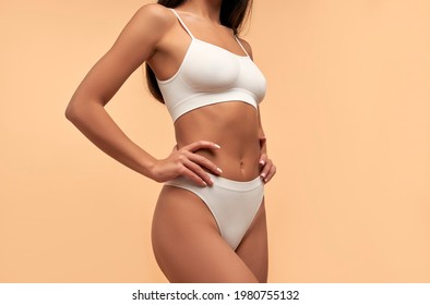 Young Asian woman in white lingerie with a toned body and a slender figure on a beige background. Laser hair removal. Plastic surgery. Sports, healthy lifestyle. Spa body care.