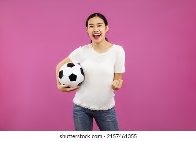 Young Asian Woman In White Shirt Holding Football Ball To Cheering A Soccer Game On The Pink Screen Background.