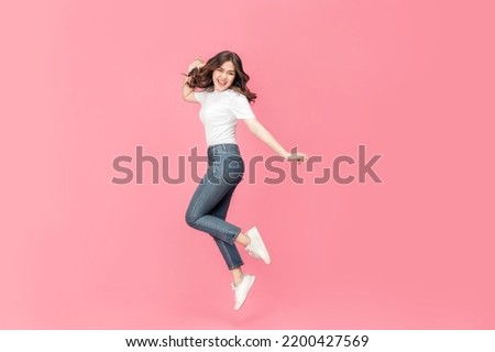 Young Asian woman in a white t-shirt cheerful expression on her face as she is very happy over something excited smile and jumping with her arm raised in air on isolated pink background. Foto d'archivio © 