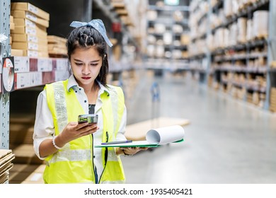 Young asian woman worker uses the phone for business contacts and holding clipboard to checking inventory in the warehouse - Powered by Shutterstock