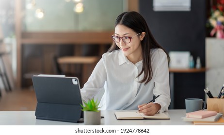 Young Asian woman working on a tablet and taking notes at the office.