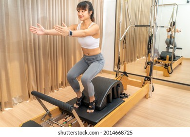 Young Asian woman working on pilates reformer machine during her health exercise training at her home gym