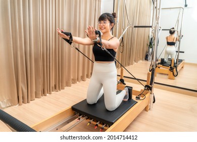 Young Asian woman working on pilates reformer machine during her health exercise training