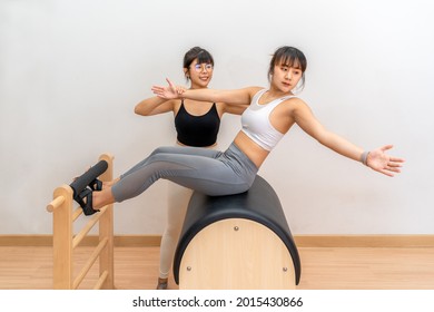 Young Asian woman working on pilates ladder barrel machine with her female trainer during her health exercise training