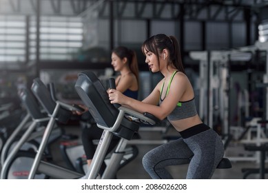 Young Asian Woman Working Out On Exercise Bike At Gym.