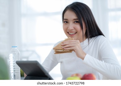 Young Asian woman working with tablet at home and eating sandwich  salad fruits at home