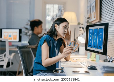 Young asian woman working as ui designer is experiencing a creative block while working on a mobile app. She is holding a color palette and looking at the computer screen - Powered by Shutterstock