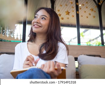 Young Asian woman or a writer sitting in a journal or writing a novel in a coffee shop outside the office. Freelance women are relaxing writing jobs. Asian women, beautiful women, Writers.
