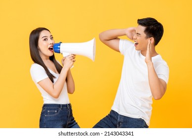 Young Asian woman yelling on megaphone to her boyfriend in studio isolated yellow color background