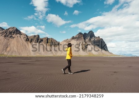 Young asian woman in yellow jacket standing on the beach with Vestrahorn mountain in viking village on Stokknes Peninsula at Southeast Iceland