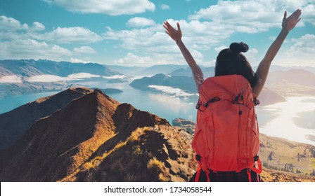 Young asian women hikers climbing up on the peak of mountain near ocean. Woman hiking in the mountains standing on a rocky summit ridge with backpack. Roys peak track, South island, New Zealand.