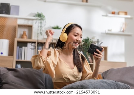 Young asian women listening to music in headphones and dancing energetic and rhythm at couch. Attractive Asian girl looking at the smart phone sitting in the living room spending leisure time at home