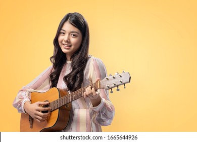A young asian women playing guitar on yellow background
