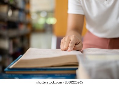 Young Asian women are searching for books and reading books on the tables and aisles of the college libraries to research and develop their academic and education self. - Shutterstock ID 2088225265