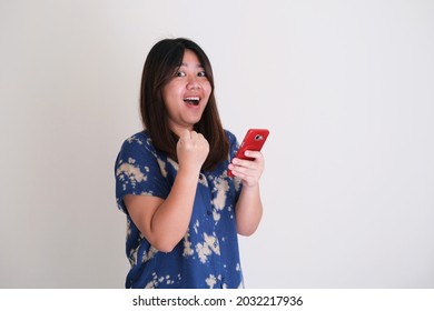 Young Asian women showing happy face expression with her fist clenched while holding a mobile phone