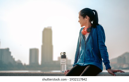 Young Asian Women Sit To Rest After Jogging A Morning Workout In The City. A City That Lives Healthy In The Capital. Exercise, Fitness, Jogging, Running, Lifestyle, Healthy Concept.