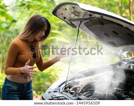 Young asian women tourist looking at the Smoke out the radiator a car, Over Heat. parked at the side of the road during the travel. Help needed. Car service. Tow service