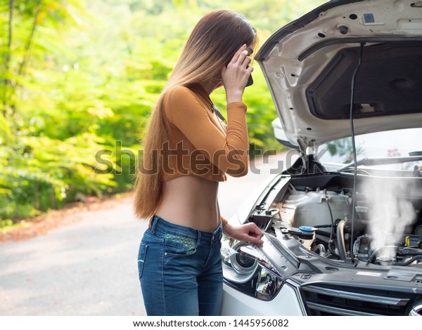 Young asian women tourist near a broken\
car on the country road is calling on smart phone Asking for Help.\
Smoke out the radiator a car, Over\
Heat