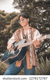 A young aspiring asian guitarist with his old guitar at a nature park or indie concert. Folk rock enthusiast. - Shutterstock ID 2278172787