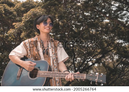 A young aspiring asian guitarist with his old guitar at a nature park or indie concert. Folk rock enthusiast.
