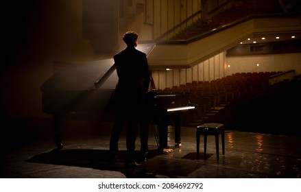 Young aspiring musician standing near grand piano on a stage of a huge concert hall - Powered by Shutterstock