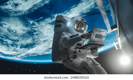 Young Astronaut Floating in Space in Zero Gravity. Spaceman Using Laptop Computer in Open Space Outside an Orbiting Spacecraft, Browsing Instruction Manuals for Maintenance Work on a Satellite