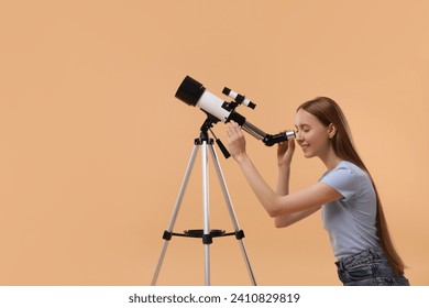 Young astronomer looking at stars through telescope on beige background, space for text
