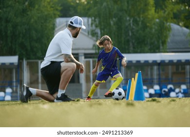 Young athlete, boy, child in uniform in motion, improving dribbling skills under watchful eye of professional coach. Outdoor training session. Concept of sport, childhood, education, active lifestyle - Powered by Shutterstock